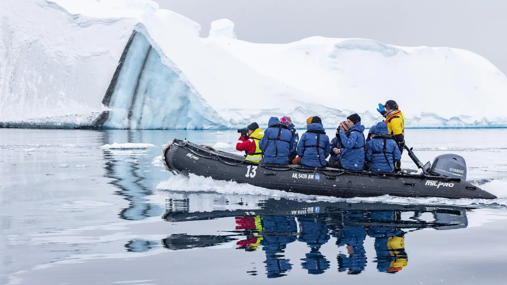 Guests in a Zodiac boat on glassy water beneath an iceberg in Antarctica